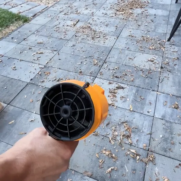 Hand holding the SuperLeafBlower over patio pavers scattered with dry leaves